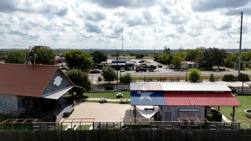 منظر لبلدة صغيرة في تكساس، يظهر مباني ذات أسطح ملونة وأعلام، مع خلفية طبيعية تتضمن أشجار وسحب في السماء.