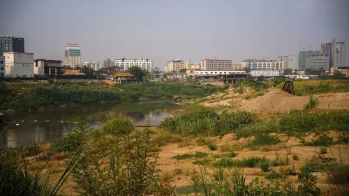 منظر لنهر يفصل بين تايلاند وميانمار، تظهر على ضفافه مبانٍ حديثة وأشجار، مما يعكس التوترات الحدودية والنشاطات الإجرامية.