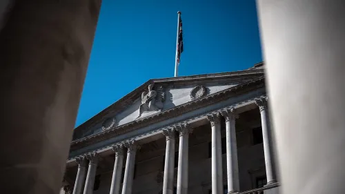 واجهة بنك إنجلترا تظهر أعمدة معمارية مميزة وعلم المملكة المتحدة يرفرف في السماء الزرقاء، تعكس التغيرات الاقتصادية الأخيرة.