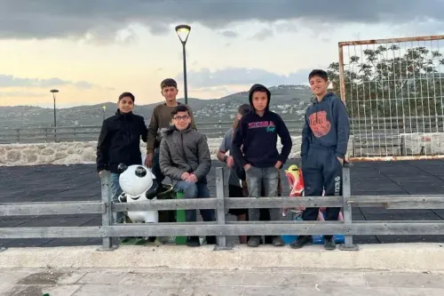 مجموعة من الأطفال والشباب في سبسطية، الضفة الغربية، يتجمعون في حديقة، في خلفية منظر طبيعي جبلي تحت سماء غائمة.