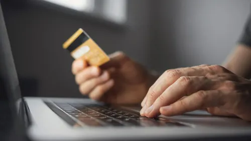 شخص يستخدم بطاقة ائتمان أثناء كتابة نص على جهاز كمبيوتر محمول، مما يعكس التفاعل مع الخدمات المالية والتقييمات الائتمانية.