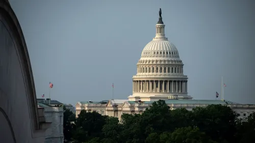 قبة مبنى الكابيتول الأمريكي تبرز في الأفق، محاطة بالأشجار، مع العلم الأمريكي يرفرف في الهواء، مما يعكس النشاط السياسي في واشنطن.