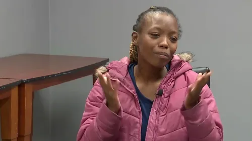 امرأة ترتدي سترة وردية تتحدث بقلق، تعبر عن معاناتها في البحث عن مأوى لعائلتها بعد فقدان طفلين بسبب التشرد في ديترويت.