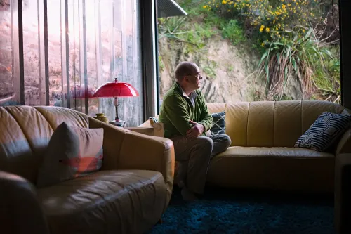 رجل مسن يجلس بمفرده على أريكة في غرفة مضيئة، يبدو عليه التأمل والقلق، مما يعكس تأثير الاكتئاب على الصحة العقلية.