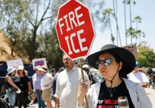 امرأة تحمل لافتة حمراء مكتوب عليها "أوقفوا ICE" خلال احتجاج ضد مداهمات الهجرة خارج ملعب دودجرز في لوس أنجلوس.