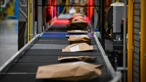 صناديق معبأة على سير متحرك في مركز توزيع أمازون، تعكس دعوة للمقاطعة ضد الشركة بسبب ممارساتها التجارية.