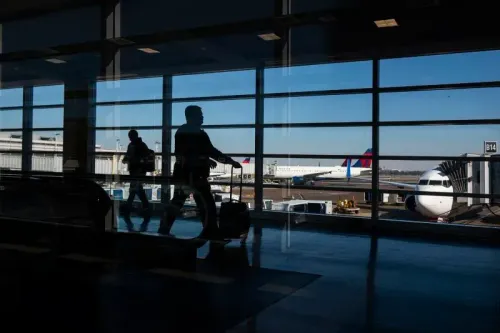 صورة لمطار يظهر فيها مسافرون يسيرون بجانب نوافذ كبيرة تطل على الطائرات، مما يعكس تأثير التضخم على طلب السفر.