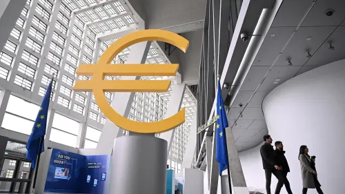 تمثال كبير لعملة اليورو في البنك المركزي الأوروبي، مع وجود أشخاص يسيرون بجانبه، يعكس تأثير التوترات التجارية على الاقتصاد الأوروبي.