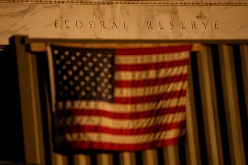 واجهة بنك الاحتياطي الفيدرالي مع علم الولايات المتحدة، تعكس التوترات الاقتصادية والسياسات النقدية في ظل التضخم.