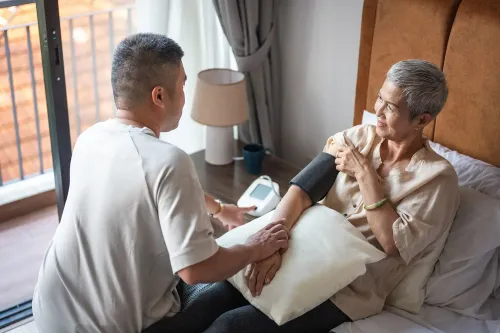 رجل يساعد امرأة مسنّة في قياس ضغط الدم داخل غرفة معيشة، مما يعكس دور مقدمي الرعاية في دعم الأهل المتقدمين في السن.