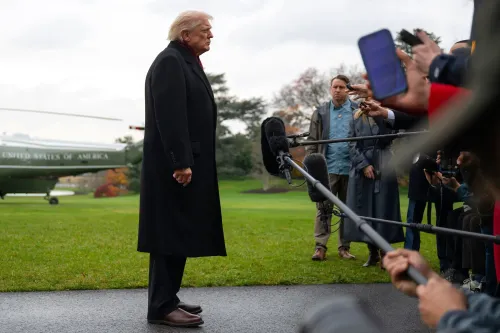 ترامب يقف جانباً خلال مؤتمر صحفي، محاطاً بالصحفيين، مع طائرة هليكوبتر في الخلفية، مما يعكس التوترات السياسية حول الرعاية الصحية.