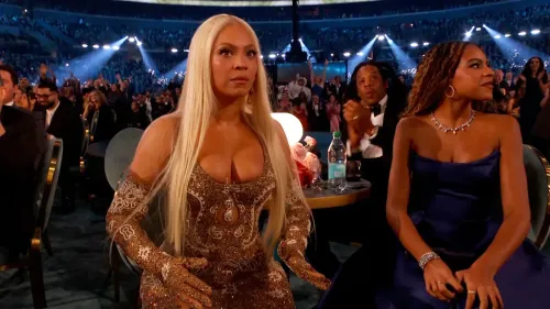 بيونسيه ترتدي فستانًا لامعًا أثناء حفل توزيع جوائز غرامي، تعبيرها يظهر التركيز والتوتر، بينما يجلس زوجها جاي زي بجانبها.