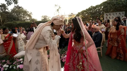 حفل زفاف فاخر في دلهي، حيث يتبادل العروسان التحية وسط أجواء احتفالية وحضور مئات الضيوف، مع زينة مزهرة وثريات متلألئة.