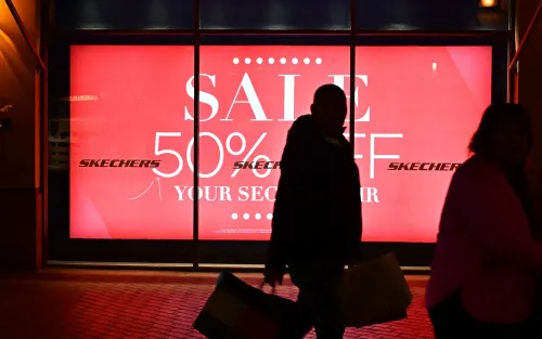 شخصان يسيران بجوار واجهة متجر تعرض لافتة حمراء كبيرة تروّج لخصم 50% على الأحذية، مما يعكس ضغوط التسوق خلال الأوقات الاقتصادية الصعبة.