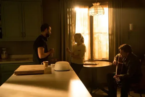 مشهد من حلقة "The Last of Us" يظهر إيلي وجويل في مطبخ مضاء بأشعة الشمس، حيث يتبادلان الحديث بينما يجلس شخص ثالث مع غيتار.