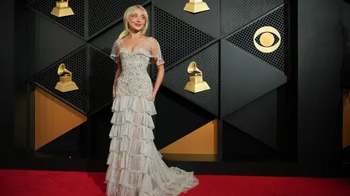 امرأة ترتدي فستاناً مزيناً بالتفاصيل اللامعة وتقف على السجادة الحمراء لحفل توزيع جوائز غرامي، مع جوائز غرامي خلفها.