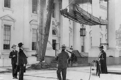 عمال يقومون بتركيب هيكل خشبي في البيت الأبيض، مع وجود معدات بناء، في سياق مشروع ترميم أو تعديل.