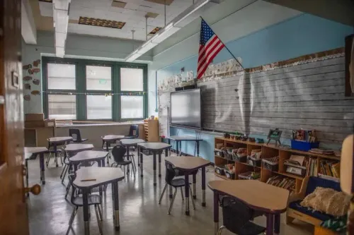 فصل دراسي فارغ يحتوي على طاولات وكراسي، مع شاشة عرض كبيرة وعلم أمريكي معلق، يعكس استخدام الذكاء الاصطناعي في التعليم.