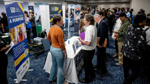 معرض توظيف مزدحم، حيث يتفاعل الباحثون عن عمل مع ممثلي الشركات، مع لافتات توضح فرص العمل المتاحة.