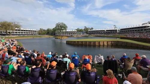 مشهد للحفرة 17 في TPC Sawgrass، حيث يتجمع الجمهور حول البحيرة المحيطة بالجزيرة الخضراء، مع أجواء تنافسية مثيرة.