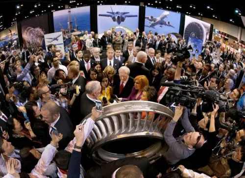 اجتماع حاشد لمساهمي بيركشاير هاثاواي مع وارن بافيت في المركز، محاطاً بالمعجبين ووسائل الإعلام، مع عرض لمعدات الشركات في الخلفية.