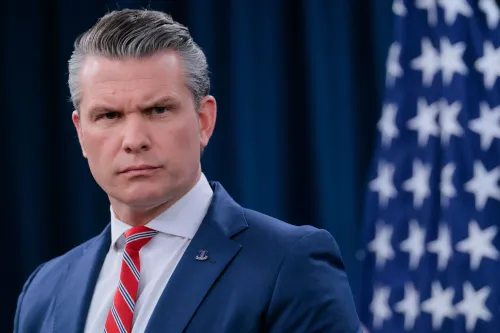 وزير الدفاع الأمريكي Pete Hegseth يتحدث بجدية، مع العلم الأمريكي خلفه، معبراً عن موقف البنتاغون بشأن استخدام الذكاء الاصطناعي في العمليات العسكرية.
