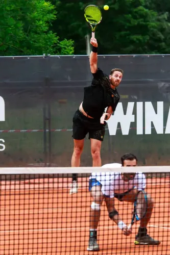 لاعب تنس يقوم بإرسال الكرة خلال مباراة على أرضية ترابية، مع التركيز على تقنياته في الإرسال السريع.