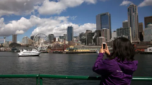 امرأة تلتقط صورة لمدينة سياتل، تظهر العجلة الدوارة والمباني الشاهقة، مما يعكس تأثير انخفاض السياحة الكندية.
