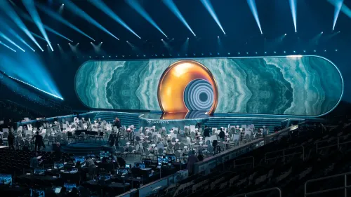 تصميم مسرح حفل توزيع جوائز غرامي مع إضاءة زرقاء وأضواء ساطعة، حيث تظهر الكراسي الفارغة في الخلفية، مما يعكس أجواء الاستعدادات للحدث.