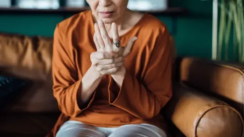 امرأة تجلس على أريكة، تمسك معصمها وتعبر عن الألم، مما يعكس تأثير الألم المزمن على الحياة اليومية.