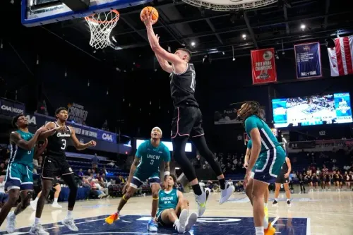 لاعب من فريق توسون يقوم بقفزة ساحقة نحو السلة خلال مباراة بطولة الرابطة الرياضية الساحلية (CAA) لكرة السلة، مع وجود لاعبين من جامعة نورث كارولينا ويلمنجتون في الخلفية.