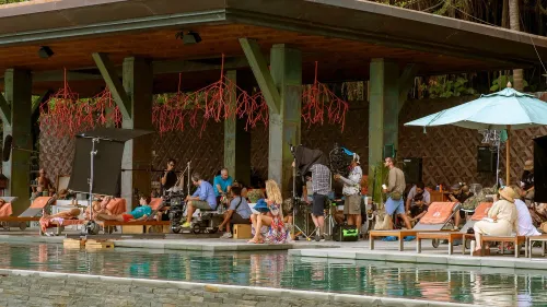 مجموعة من طاقم تصوير مسلسل "اللوتس الأبيض" أثناء العمل بجوار المسبح، مع إعدادات تصوير ومشاهدين في خلفية المكان.