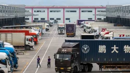 ساحة شحن مزدحمة بالشاحنات في منطقة تجارية، تعكس تأثير التعريفات الجمركية على التجارة الدولية.