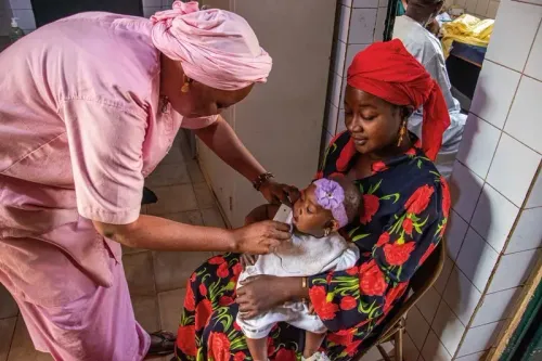 امرأة ترتدي ملابس تقليدية تحمل طفلاً بينما تقوم مربية بفحص صحة الطفل في مركز طبي، في سياق جهود مكافحة سوء التغذية في نيجيريا.