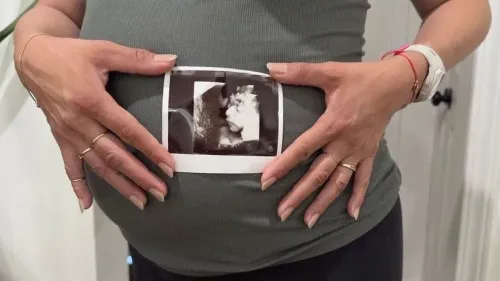 امرأة حامل ترتدي قميصًا رماديًا، تمسك بصورة بالأشعة فوق الصوتية لطفلها، تعبر عن القلق بشأن الجنسية في ظل التغييرات القانونية.