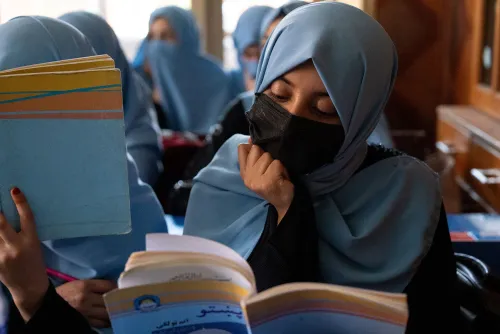 طالبة ترتدي حجابًا وتقرأ كتابًا في مدرسة دينية للبنات في كابول، تعكس تحديات التعليم تحت حكم طالبان.
