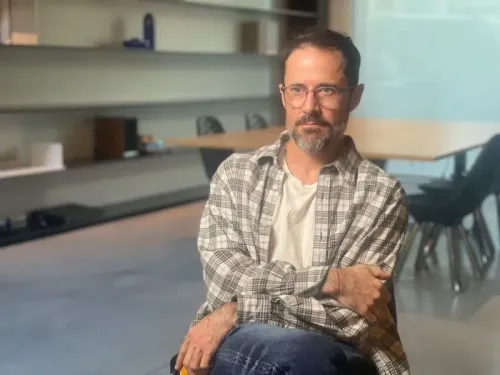 شخص يجلس في مكتب حديث، يرتدي نظارات وقميصاً مخططاً، مع تعبير جاد، يعكس التحديات التي واجهتها تويتر في تطورها.