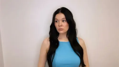 امرأة ذات شعر أسود طويل ترتدي قميصًا أزرق، تبدو مشوشة وتعبر عن القلق. الصورة تعكس المخاوف المتزايدة بين حاملي البطاقة الخضراء في الولايات المتحدة.