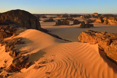 منظر لصخور عملاقة وكثبان رملية في الصحراء الجزائرية الكبرى، حيث يبرز جمال الطبيعة الفريد وتضاريسها المذهلة.