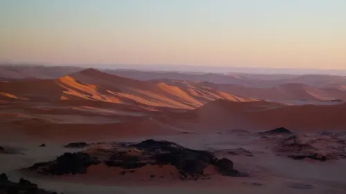 منظر لصحراء الجزائر الكبرى عند الغسق، حيث تتداخل الكثبان الرملية مع الصخور، مما يبرز جمال الطبيعة الفريد في المنطقة.