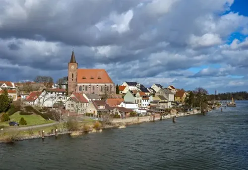 منظر لبلدة آيزنهوتنشتات في شرق ألمانيا، تظهر المنازل الملونة بجانب نهر أودر مع كنيسة بارزة في الخلفية، تعكس الطابع المعماري الفريد للمدينة.