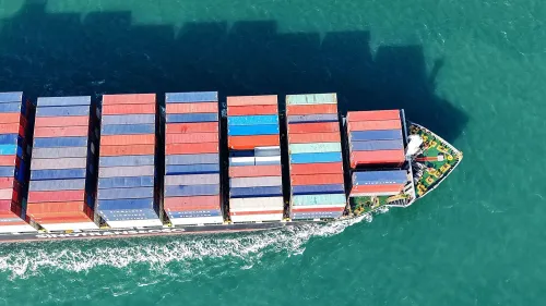 سفينة شحن محملة بالحاويات الملونة تبحر في المياه، مما يبرز تأثير التعريفات الجمركية على التجارة العالمية.