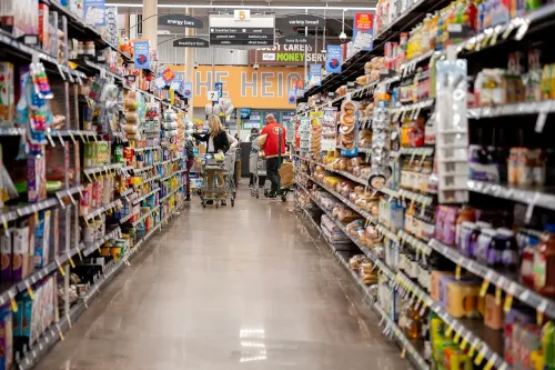 ممر في سوبرماركت يظهر متسوقين يتجولون بين الرفوف المليئة بالمنتجات، مما يعكس حالة الإنفاق الاستهلاكي في الاقتصاد الأمريكي.