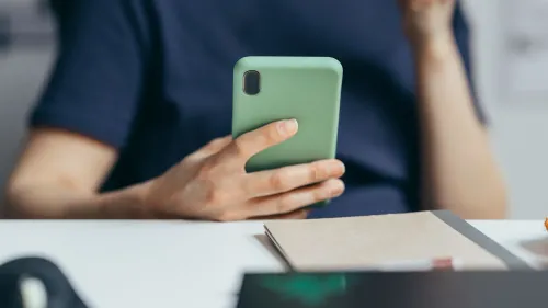 شخص يستخدم هاتفًا ذكيًا بلون أخضر في يده، محاطًا بمكتب يحتوي على أوراق، مما يعكس موضوع المعلومات المضللة والتواصل الرقمي.