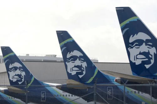 ذيل طائرات Alaska Airlines متوقفة في مطار مع خلفية مبنى، تعكس موضوع اضطرابات الركاب وتأخير الرحلات الجوية.