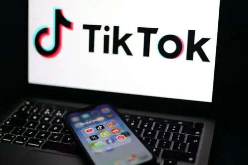 شاشة كمبيوتر محمول تعرض شعار TikTok، مع هاتف ذكي بالقرب منها يحتوي على أيقونات تطبيقات وسائل التواصل الاجتماعي، مما يبرز قضايا إدمان الشباب.