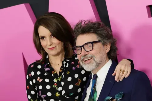 تينا فاي وجيف ريتشموند يتبسمان معًا في حدث عام، بينما يرتديان ملابس أنيقة، مع خلفية وردية تضيف لمسة مرحة.