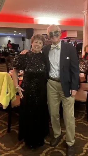 زوجان يرتديان ملابس أنيقة في احتفال، حيث ترتدي المرأة فستانًا أسود لامعًا بينما يرتدي الرجل بدلة مع ربطة عنق.