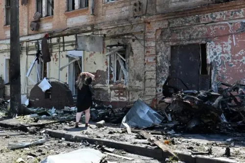 امرأة تقف في موقع دمار نتيجة الهجمات في أوكرانيا، حيث تظهر خلفها جدران متهدمة وحطام سيارات، مما يعكس آثار النزاع المستمر.