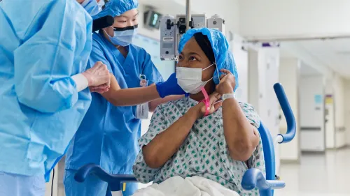 امرأة ترتدي زي المستشفى وتستعد لعملية زراعة كلية خنزير، محاطة بمقدمي الرعاية الصحية في بيئة طبية.